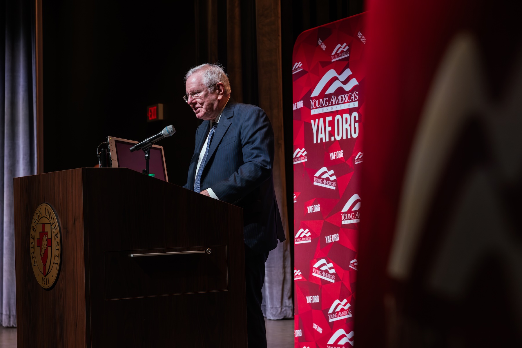 Steve Forbes speaking at an Anderson University podium on stage