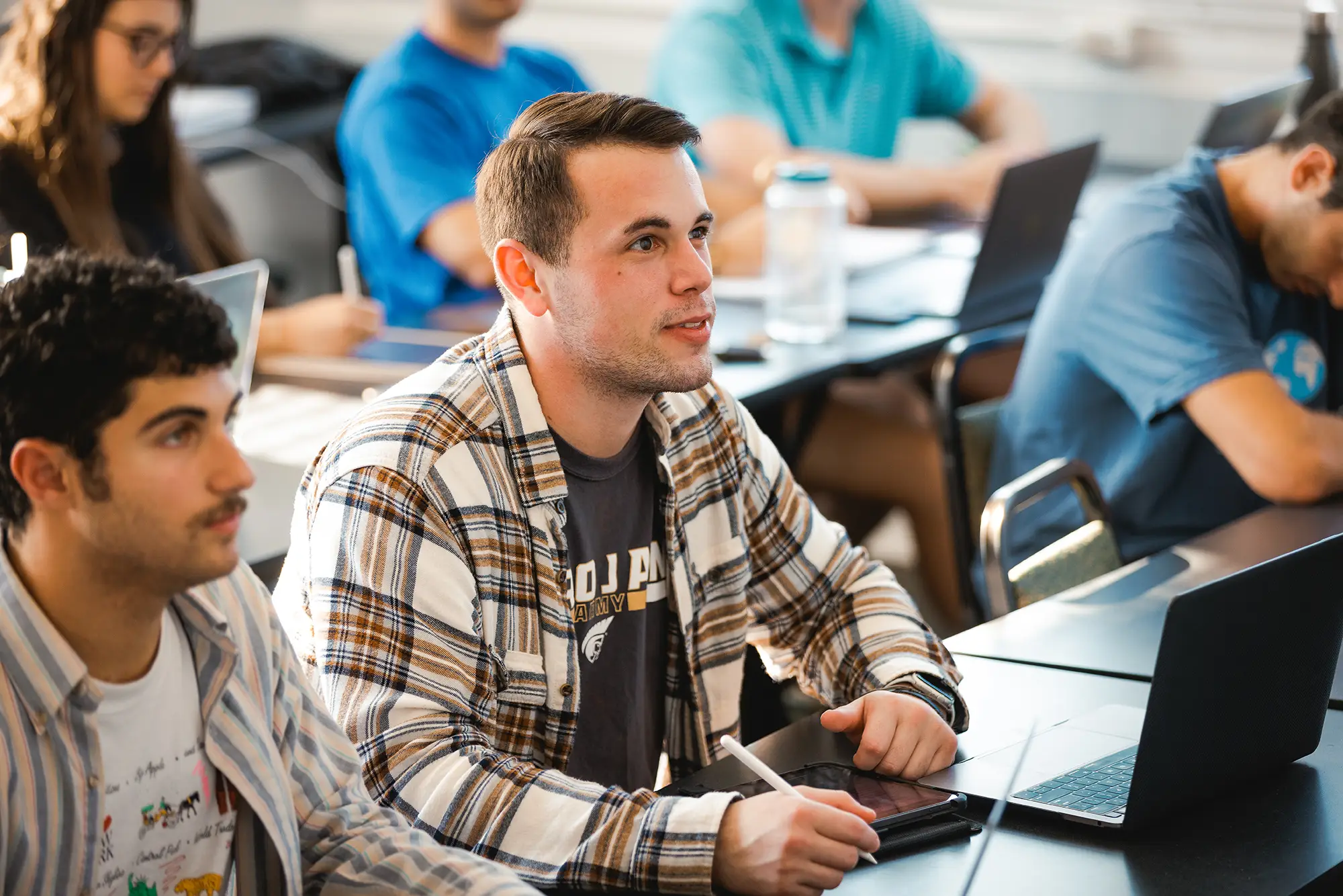An engaged Anderson University student taking notes on a tablet during class alongside fellow students.